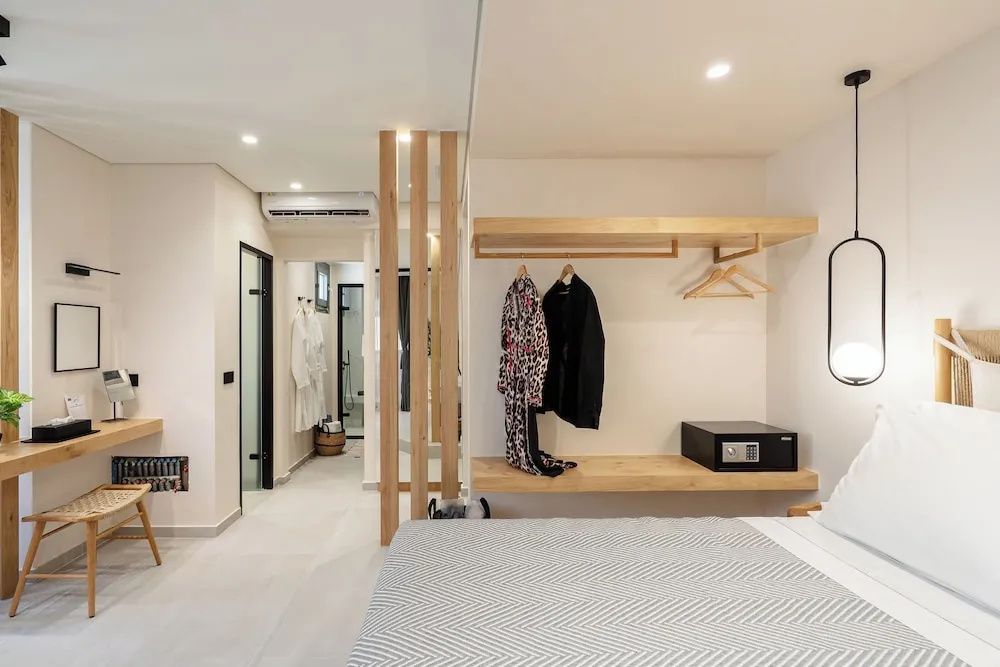 Offene Garderobe aus Holz mit Bügeln und Safe sowie ein Durchgang zum Bad mit Bademänteln.