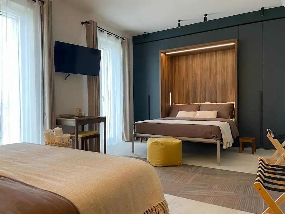 Ein Bett vor einer dunklen Schrankwand mit Holzpaneel neben einem gelben Sitzpouf.