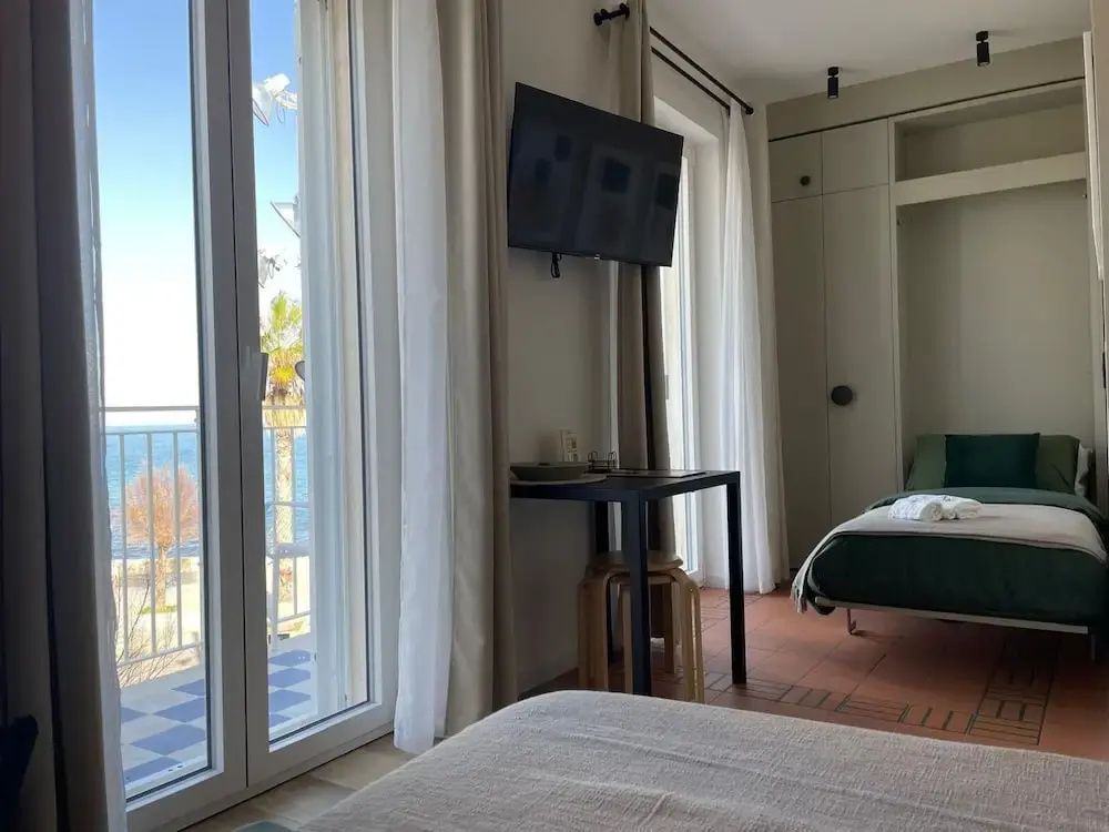 Hell eingerichtetes Hotelzimmer mit Blick durch die Balkontür auf das Meer und Palmen.