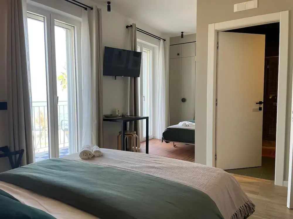 Doppelbett mit grüner Tagesdecke in einem modernen Zimmer mit Balkon und Meerblick.