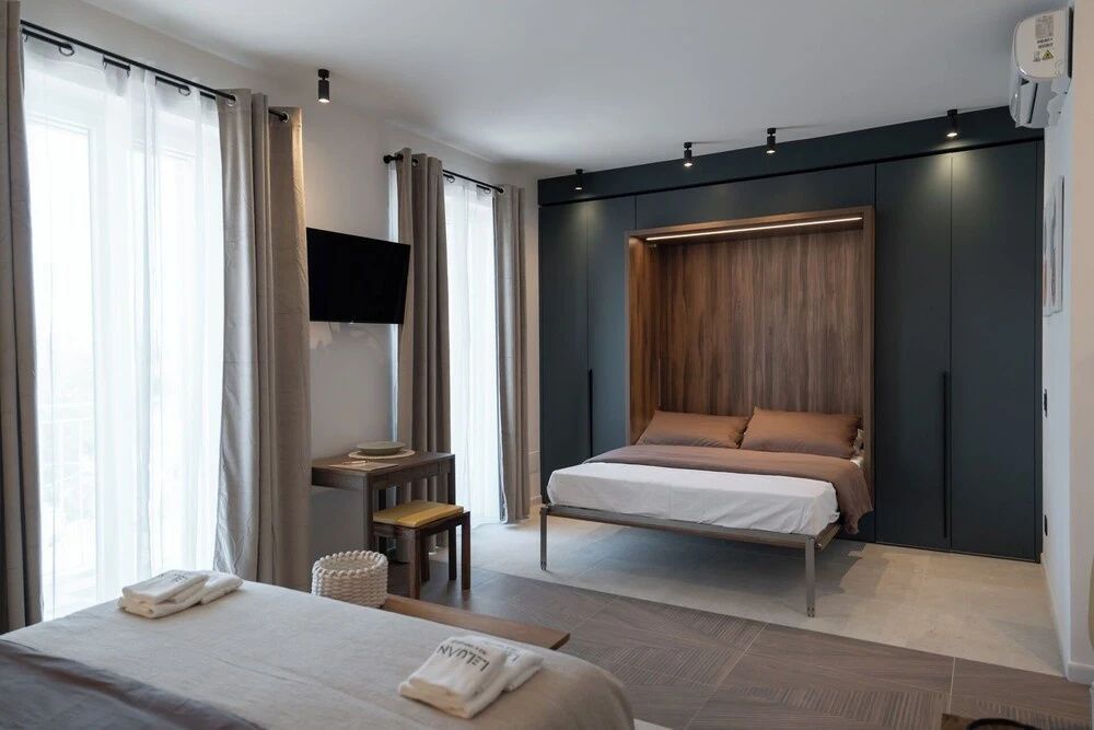 Geräumiges Schlafzimmer mit ausgefahrenem Wandbett und Vorhängen vor Fenstern.