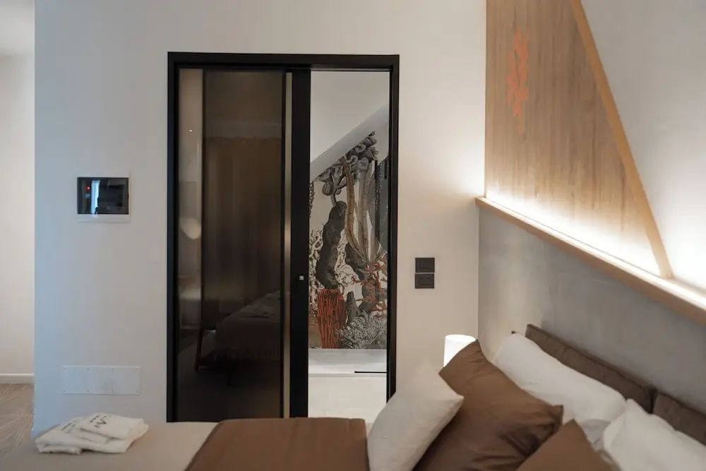 Schlafzimmer mit Doppelbett und Blick durch die geöffnete Schiebetür in das Badezimmer.
