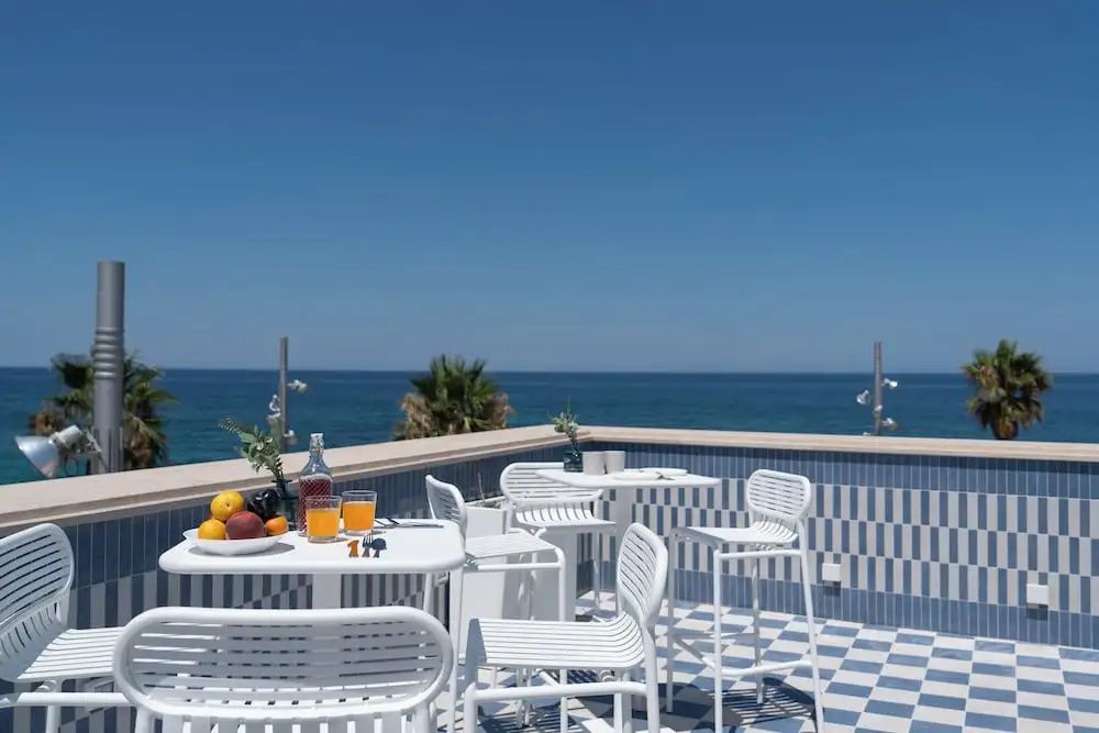 Dachterrasse mit weißen Tischen, Stühlen und Blick auf das blaue Meer.