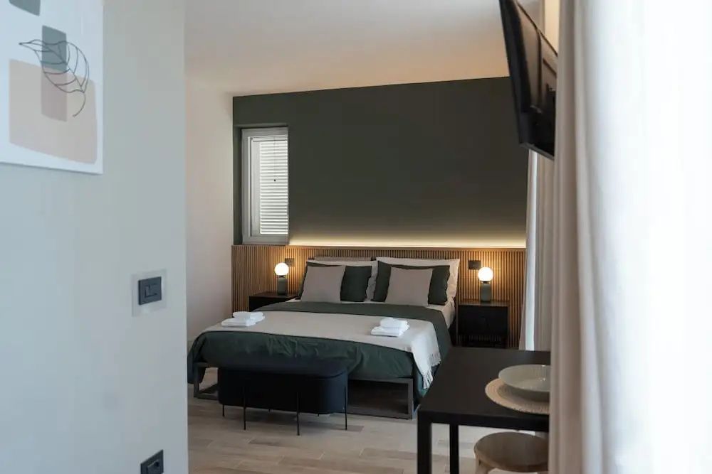 Doppelbett mit dunkler Akzentwand, Holzpaneel und indirekter Beleuchtung im Schlafbereich.