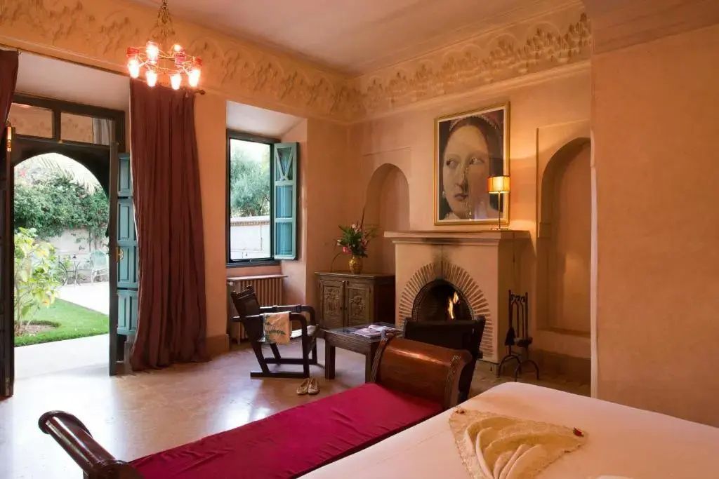 Elegantes Hotelzimmer mit brennendem Kamin, Holzstuhl, roter Liege und klassischem Wandbild.