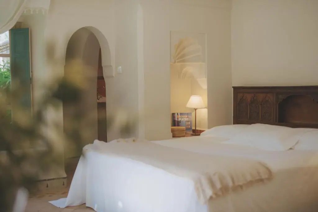 Schlafbereich mit weiß gepolstertem Bett, Nachttischlampe und einem traditionellen Wandbogen.