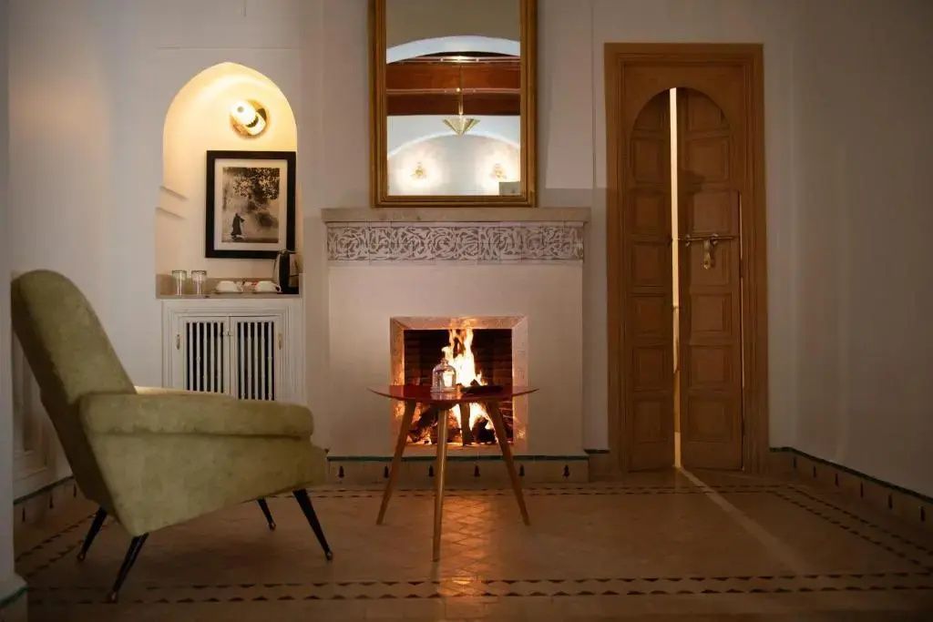 Wohnbereich mit brennendem Kamin, Spiegel, Sessel und einer verzierten Holzstiltür.