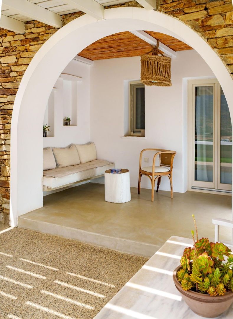 Überdachte Terrasse mit Rundbogen, heller Sitzbank, Holzstuhl und Steinwand.