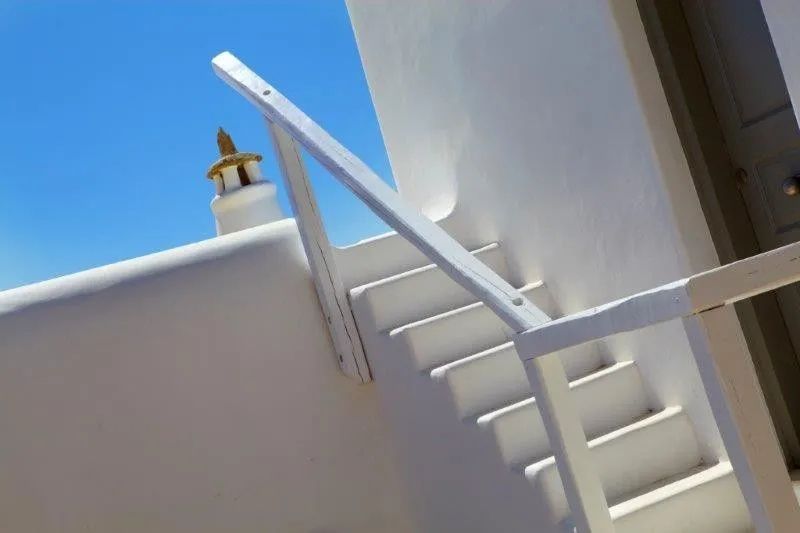 Weiß getünchte Außentreppe an einem Gebäude im kykladischen Stil unter blauem Himmel.