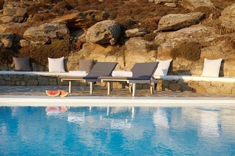 Zwei Sonnenliegen stehen am Rand eines Swimmingpools vor einer felsigen Naturkulisse.