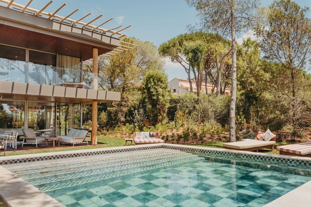 Außenansicht des Hotelgebäudes mit modernem Pool, Holzterrasse und Gartenanlage.