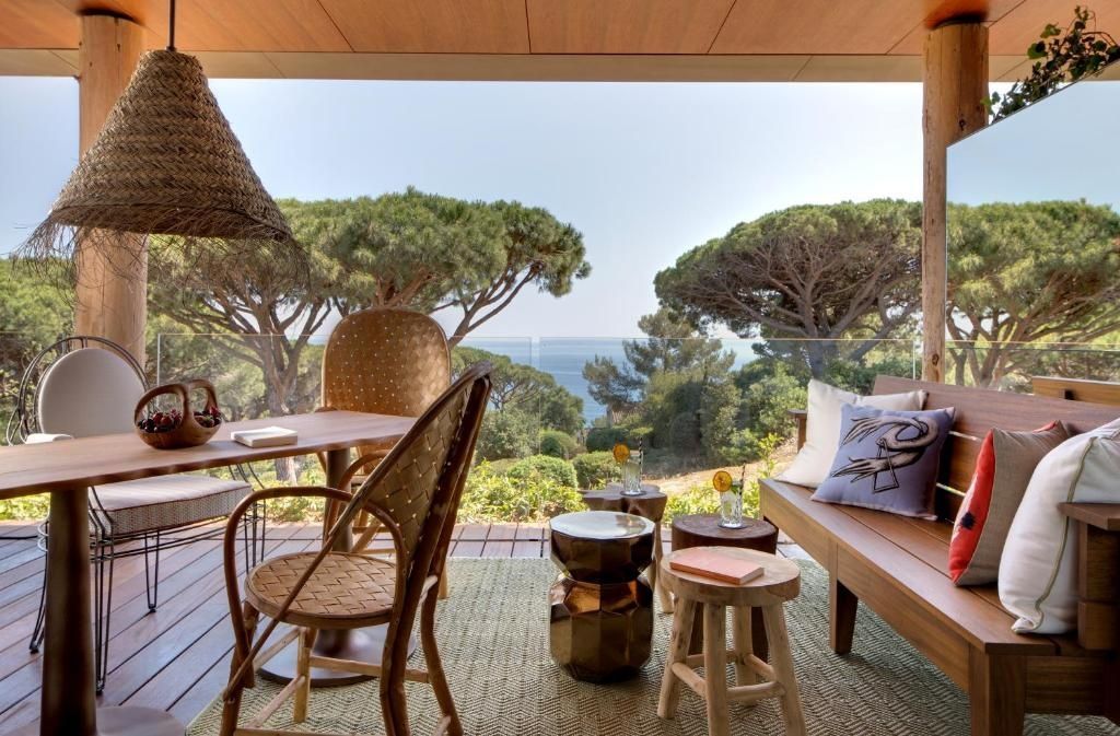 Möblierter Balkon mit Stühlen, Tisch und Ausblick auf das Meer durch Pinien.