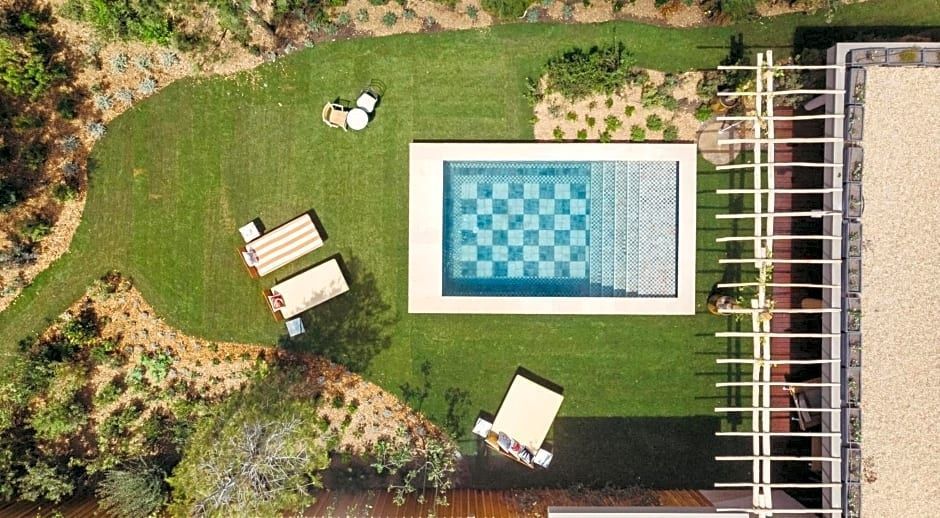Vogelperspektive auf einen rechteckigen Pool im grünen Garten mit Sonnenliegen.