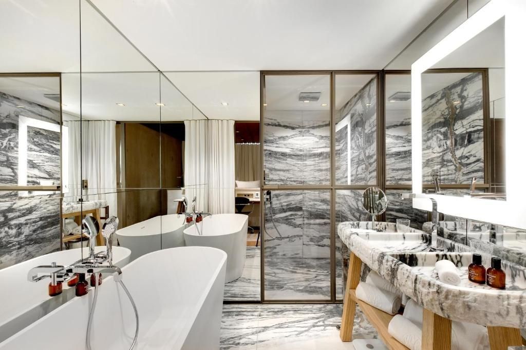 Marmorierte Wände im Badezimmer mit einer freistehenden Badewanne, gläserner Dusche und zwei Waschtischen.