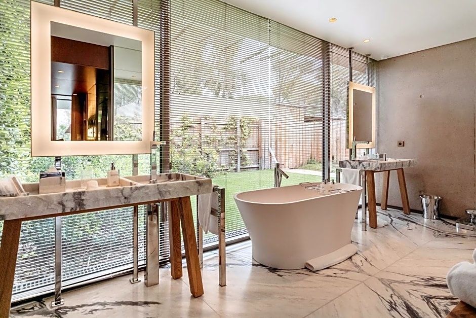 Badezimmer mit freistehender Badewanne, zwei Waschtischen und bodentiefen Fenstern ins Grüne.