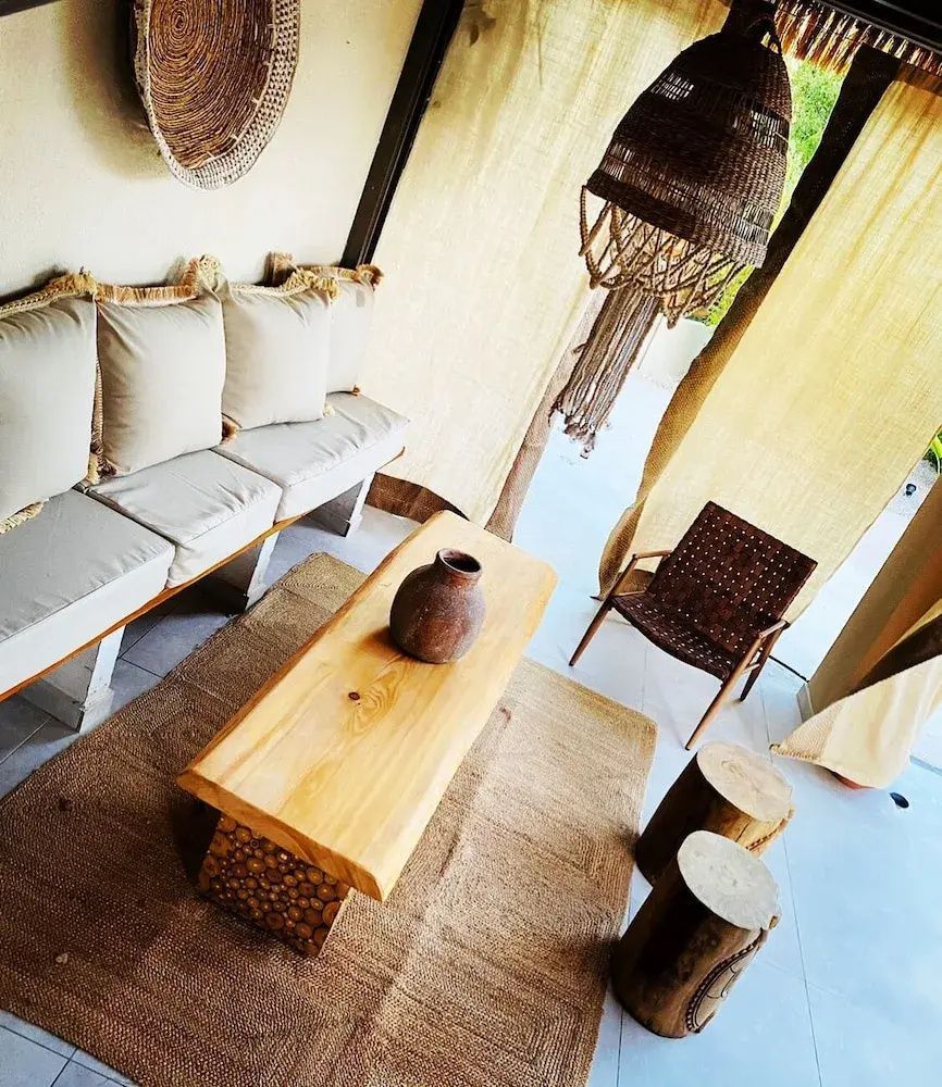 Sitzecke im Boho Stil mit Holzbank, heller Bepolsterung und einem Holzcouchtisch.