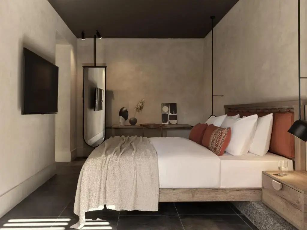 Hotelzimmer mit Doppelbett, dunkler Decke, modernem Spiegel und hellem Holzschreibtisch.