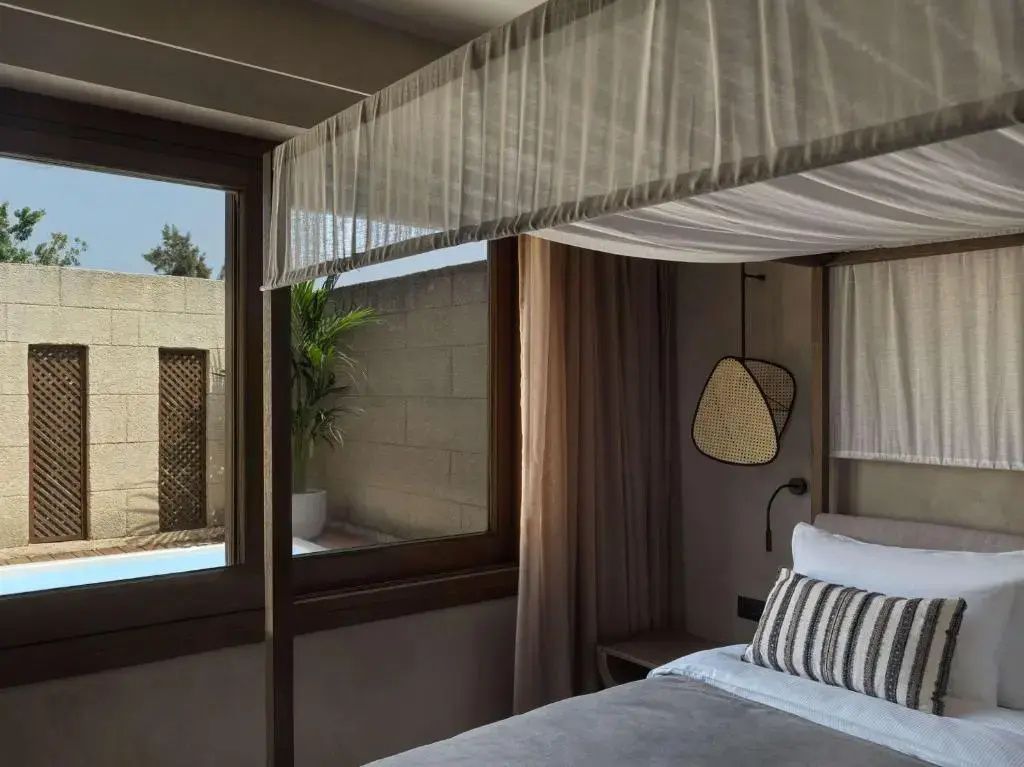 Himmelbett in einem hellen Hotelzimmer mit Blick durch das Fenster nach draußen.