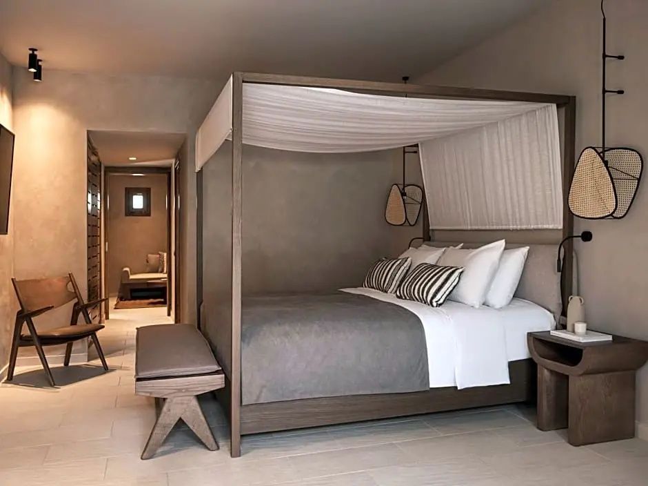 Doppelbett mit hölzernem Baldachinrahmen, Kissen und einer Holzbank im Hotelzimmer.