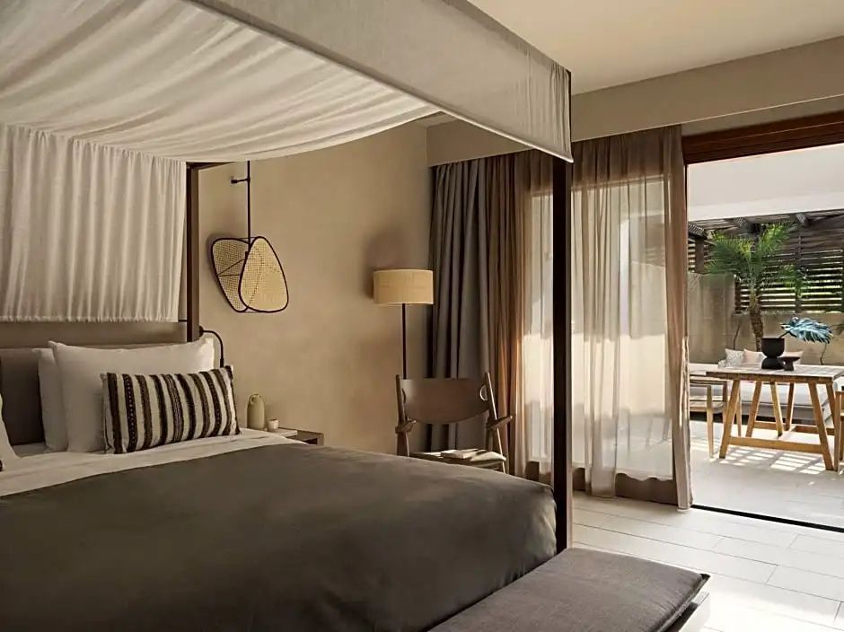 Helles Hotelzimmer mit Baldachinbett und Zugang zur Terrasse mit Sitzgelegenheiten.