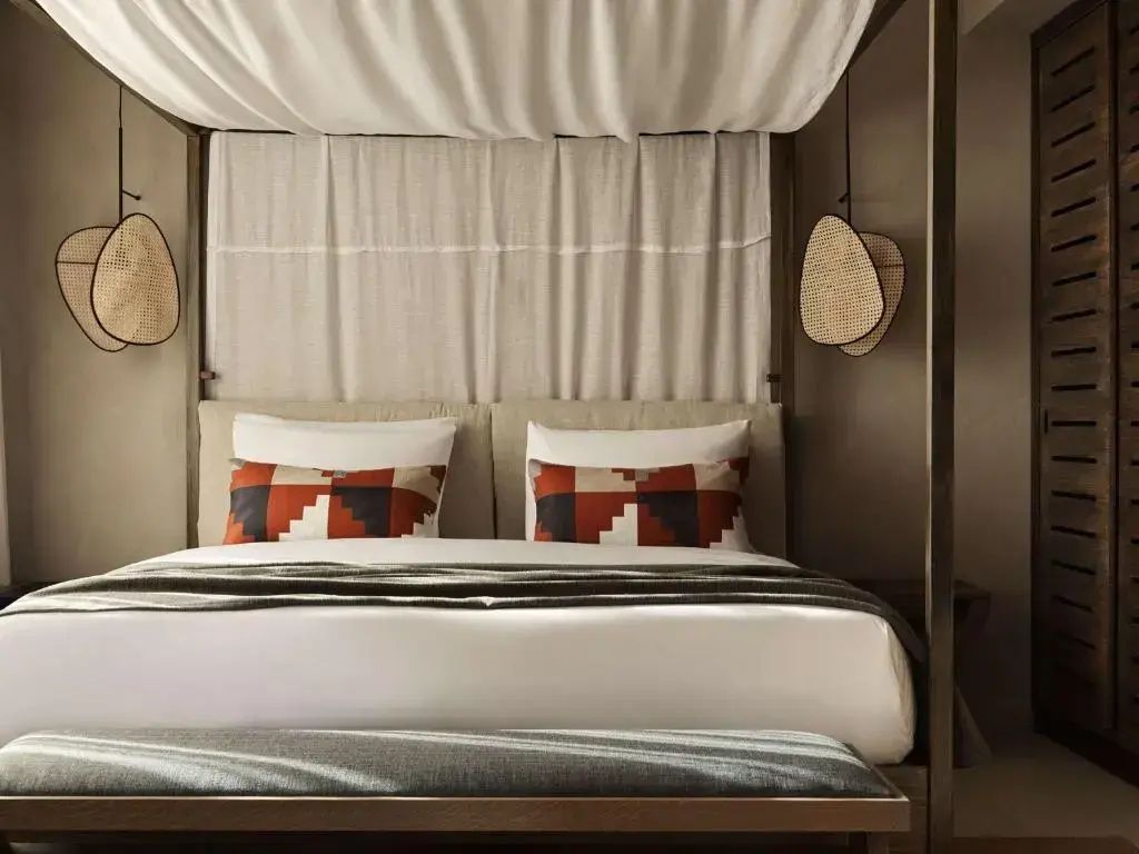 Doppelbett mit Baldachin, gemusterten Kissen und Holzrahmen im Hotelzimmer.