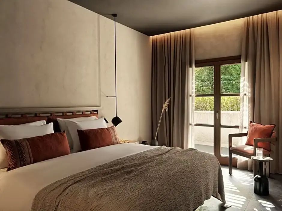 Hell eingerichtetes Schlafzimmer mit Doppelbett, Kissen in Erdtönen und Balkontür ins Grüne.