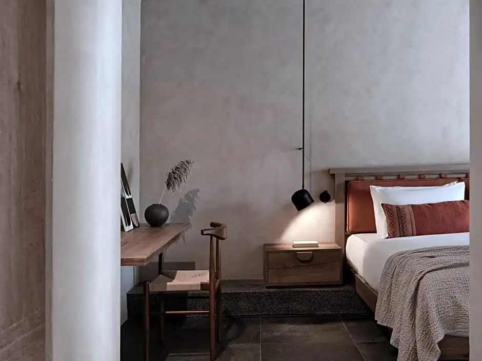 Arbeitsbereich im Hotelzimmer mit Holztisch, Stuhl und Bett mit Nachttischlampe.