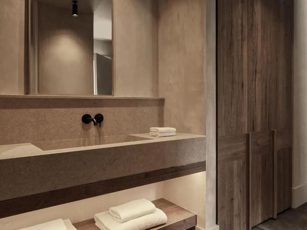 Badezimmer mit Steinwaschbecken, schwarzer Armatur, Spiegel und zusammengerollten Handtüchern.