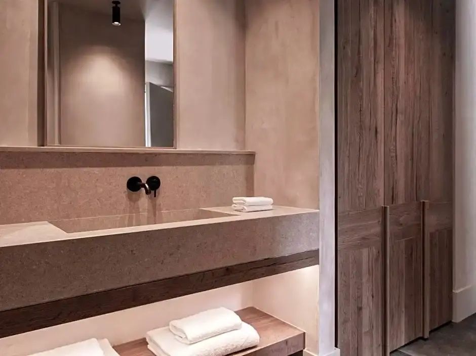 Badezimmer mit Steinwaschbecken, schwarzer Armatur, gefalteten Handtüchern und Holzschrank.