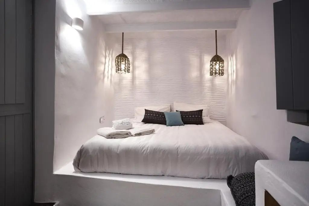 Weiß gestaltetes Schlafzimmer mit einem Doppelbett in einer Wandnische und Hängelampen.