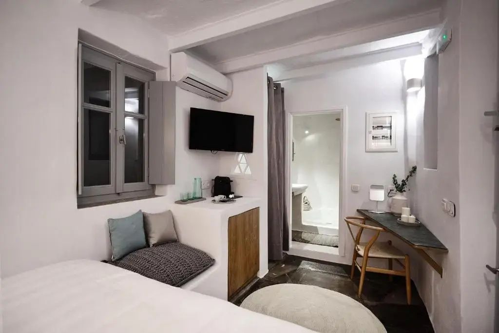 Hell eingerichtetes Hotelzimmer mit Fernseher, Schreibtisch und Durchgang zum Badezimmer.