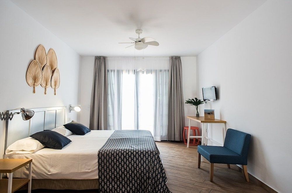 Schlafbereich mit Doppelbett, Deckenventilator, Schreibtisch und Sitzgelegenheit.