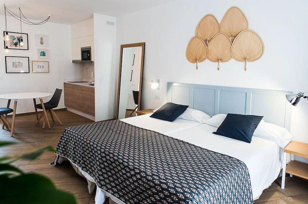 Doppelbett mit Wanddekoration, Standspiegel und angrenzender Küchenzeile.