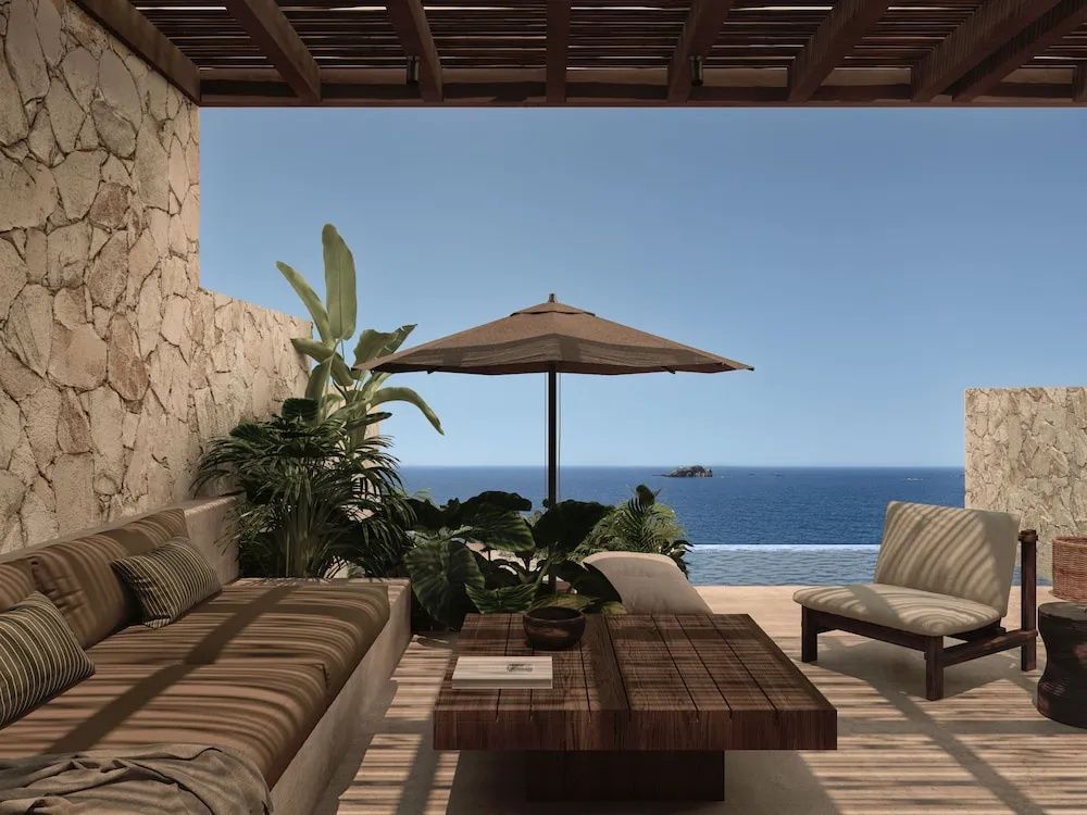 Terrasse mit Holzmöbeln, Sonnenschirm und Blick auf das blaue Meer unter klarem Himmel.