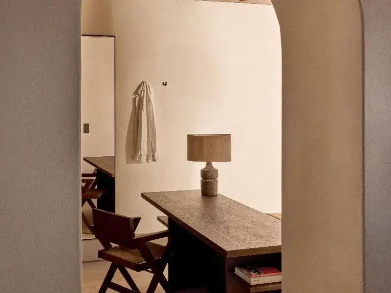Schreibtisch aus Holz mit Tischleuchte und Holzstuhl in einem hellen Zimmer.