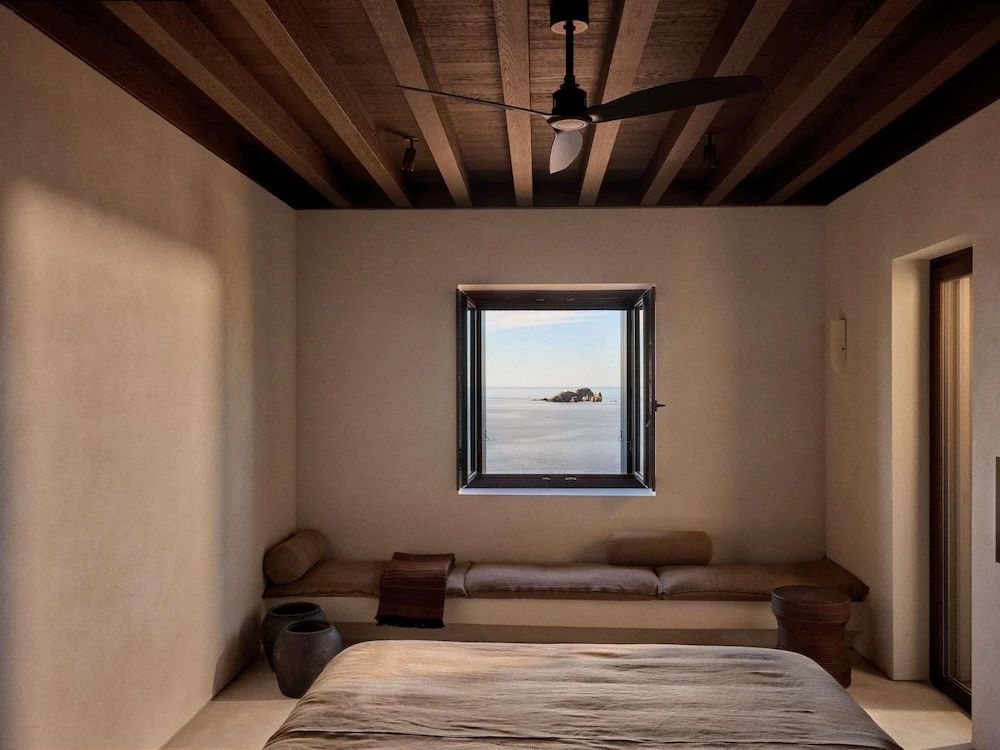 Schlafzimmer mit Blick durch ein Fenster auf das Meer und eine kleine Felseninsel.