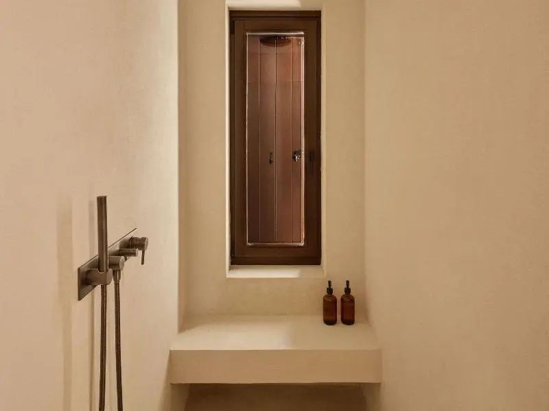 Dusche im Badezimmer mit heller Sitzbank, schmalem Fenster und dunkler Armatur.