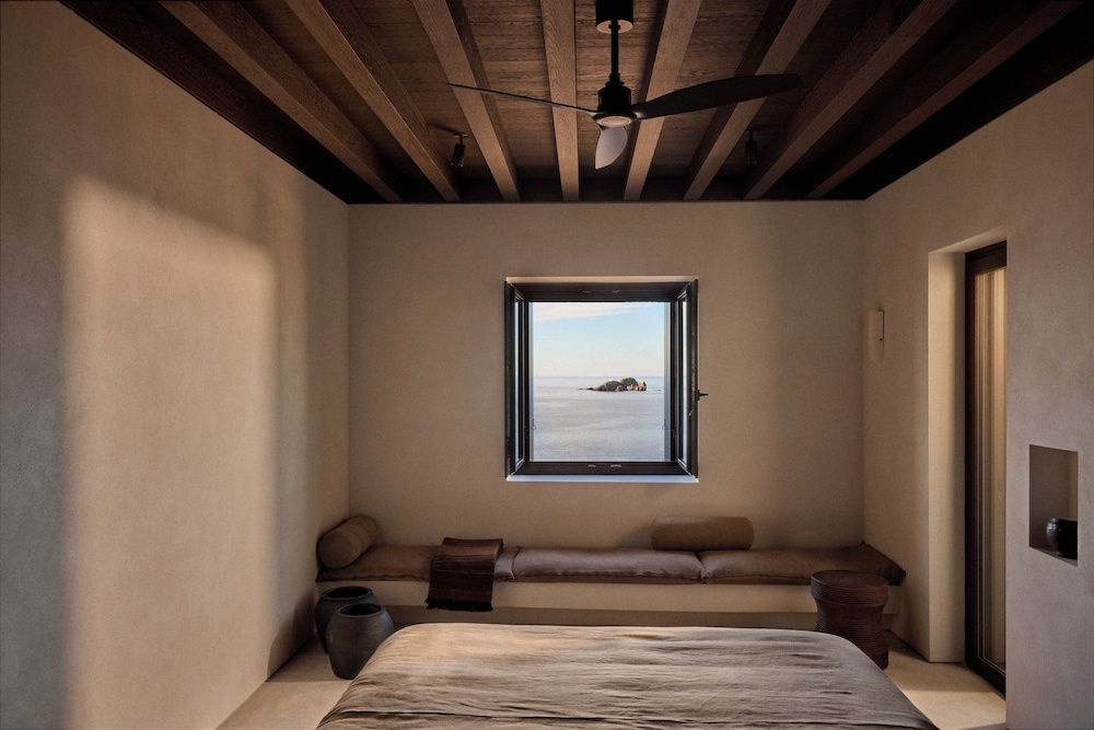 Schlafzimmer mit Holzbalkendecke, Ventilator und Fenster mit Blick auf das Meer.