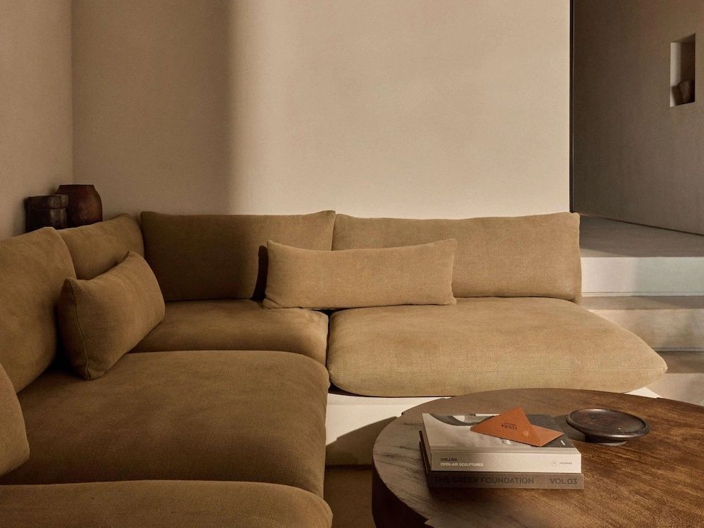 Beigefarbenes Ecksofa mit Kissen und runder Couchtisch aus Holz.