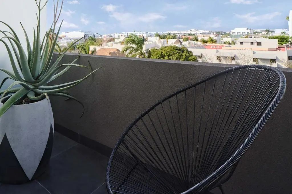 Blick vom Balkon mit schwarzem Sessel auf die umliegenden Gebäude und Palmen.