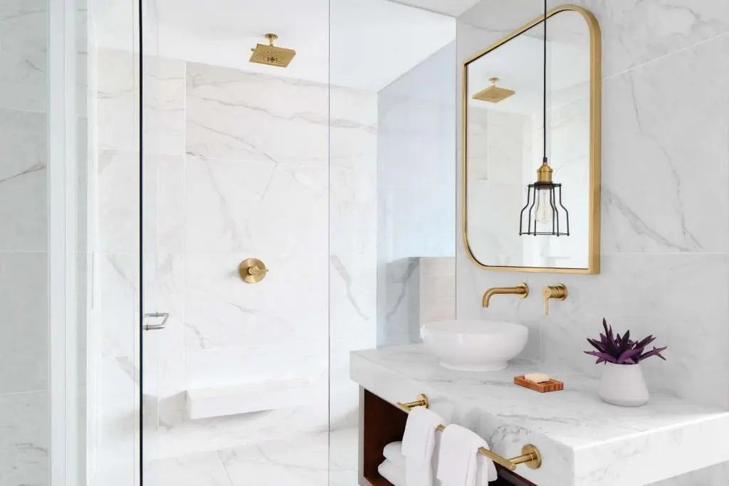 Badezimmer mit Marmorwaschtisch, goldenen Armaturen und moderner Dusche hinter Glas.