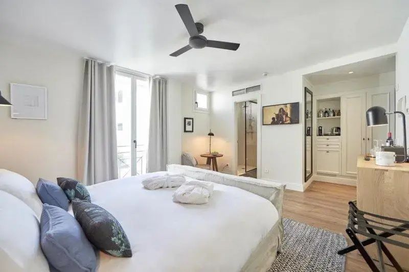 Helles Hotelzimmer mit großem Doppelbett, weißer Bettwäsche, Deckenventilator und Zugang zum Bad.