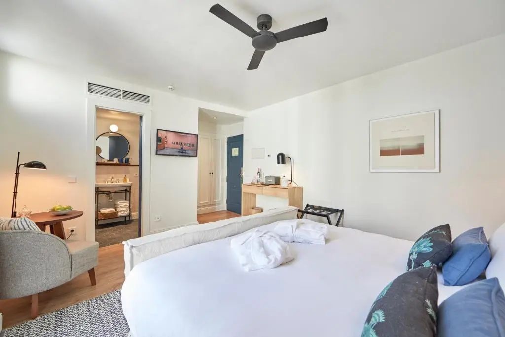Doppelbett mit zwei Bademänteln, Deckenventilator und angrenzendem Badezimmer.