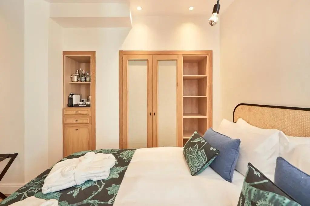 Bett mit Kissen im Vordergrund und ein Holzschrank mit integrierter Minibar dahinter.