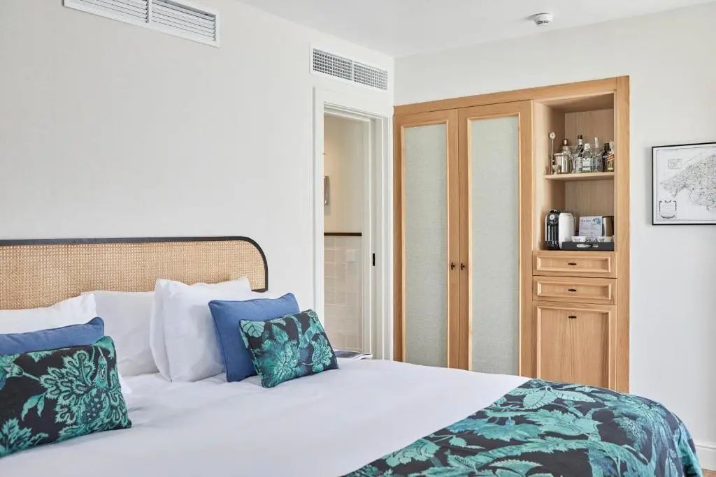 Bett mit blauen und gemusterten Kissen vor Holzschrank und Durchgang zum Bad.