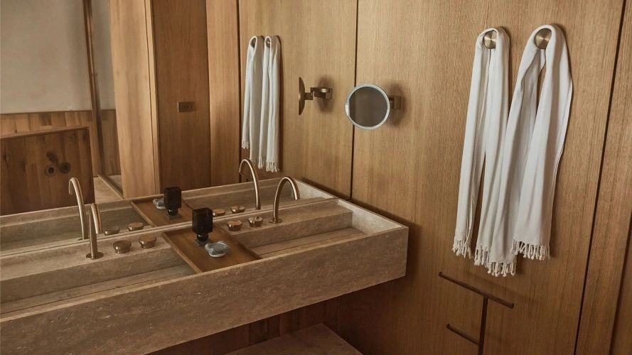 Waschbecken aus Naturstein mit Armaturen aus Messing an einer Holzverkleidung.