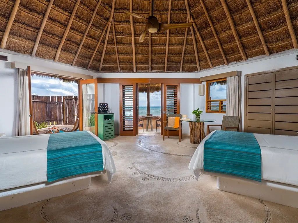 Zimmer mit Reetdachdecke, zwei Einzelbetten und Blick durch geöffnete Türen aufs Meer.