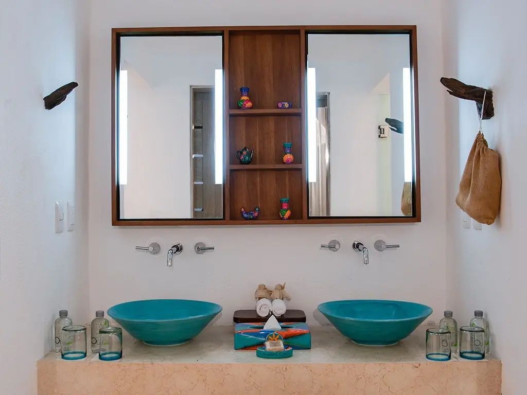 Badezimmer mit zwei türkisfarbenen Aufsatzwaschbecken und beleuchtetem Doppelspiegel.