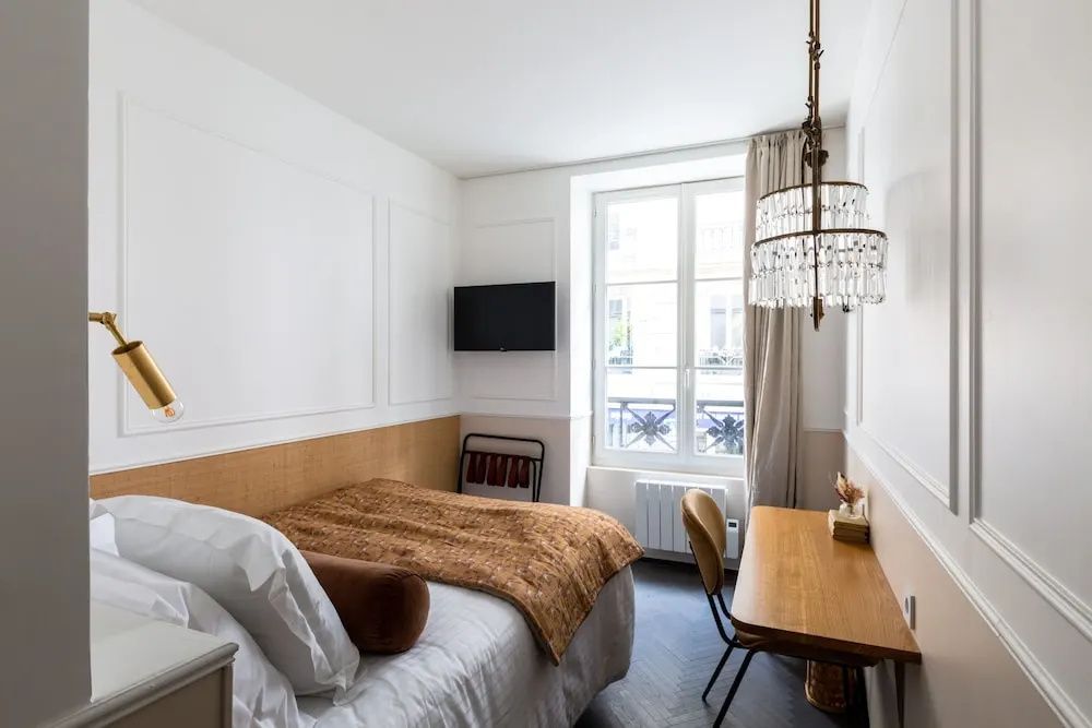 Einrichtung eines Hotelzimmers mit Bett, Fernseher, Schreibplatz und Fenster mit Blick nach draußen.