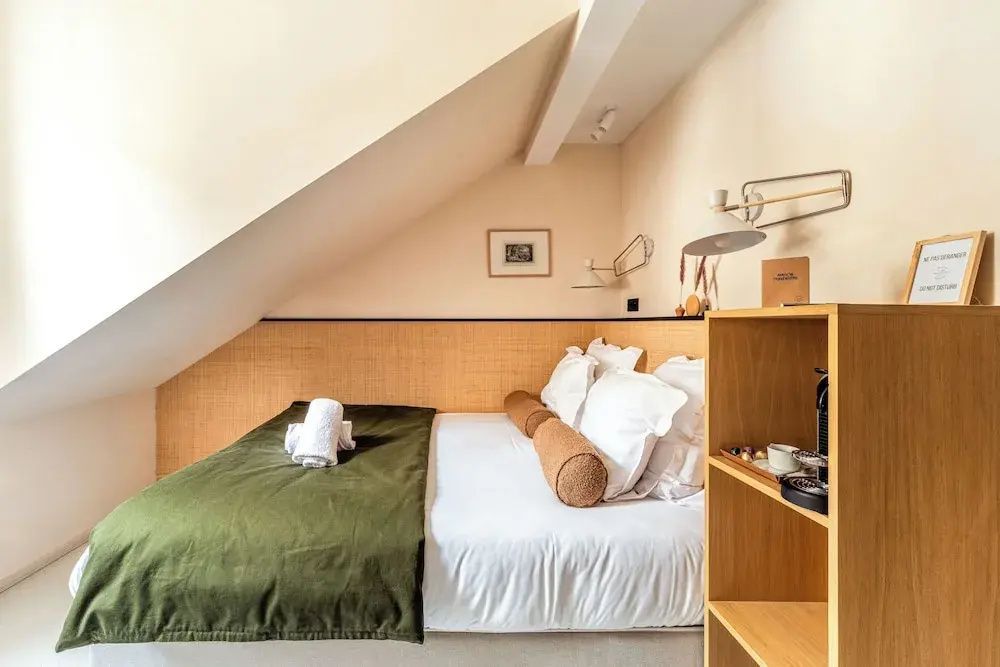 Hotelzimmer unter einer Dachschräge mit Doppelbett, grüner Tagesdecke und offenem Regal.